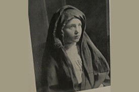 Black and white photo of a small girl with a cape wrapped around her including a hood.